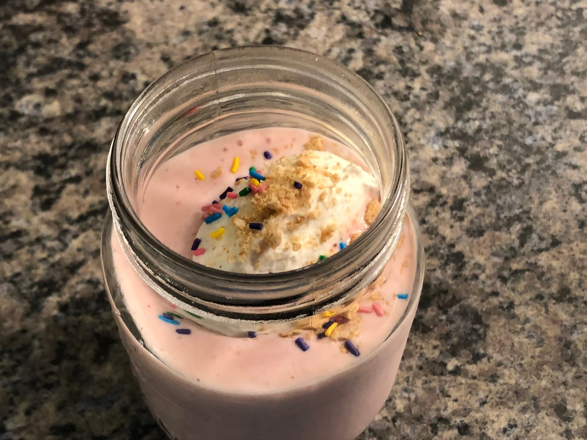 Strawberry cheesecake smoothie in a glass jar topped with whipped cream and colorful sprinkles.