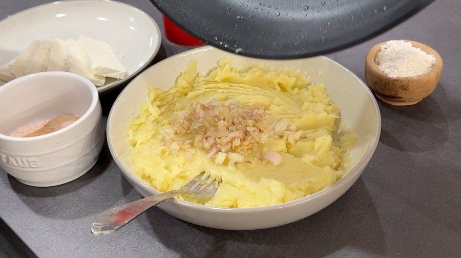 Mashed potatoes with sautéed shallots in a white bowl, ready to be formed into potato pancakes.