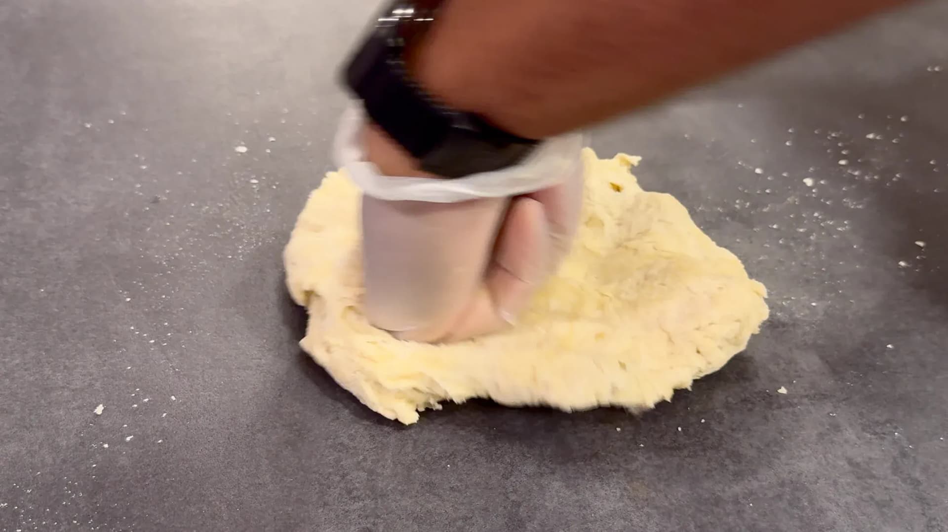 Hands kneading yellow dough on a dark countertop with a clear bowl nearby.