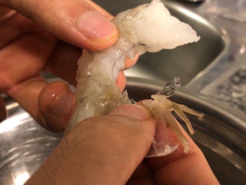 Hands demonstrating how to remove the tail from a cooked shrimp by pinching and pulling the shell down.