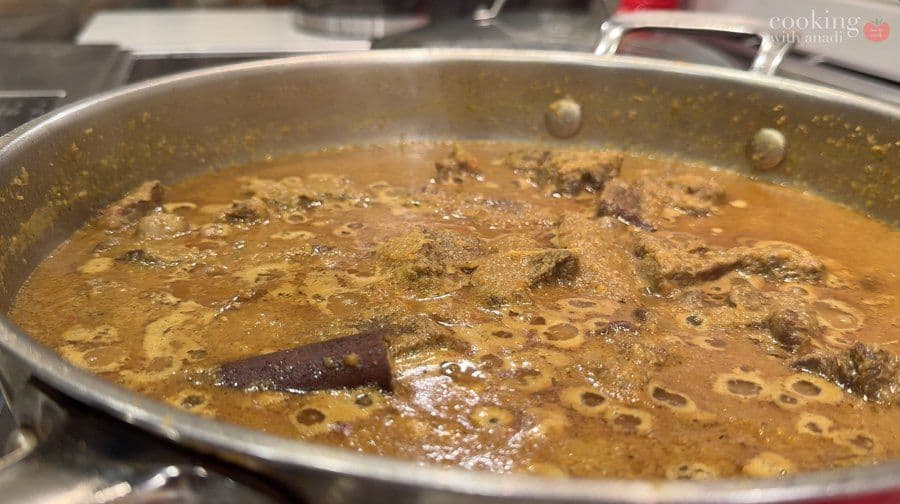 Beef rendang simmering in a large pot with rich brown sauce and a red chili visible in the curry.