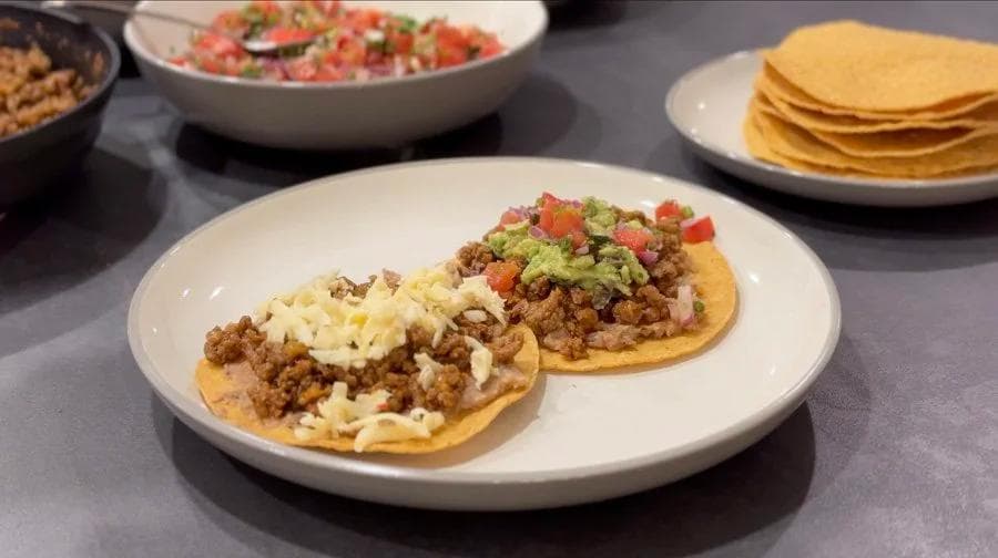Two loaded beef tostadas topped with shredded cheese and pico de gallo on a white plate.