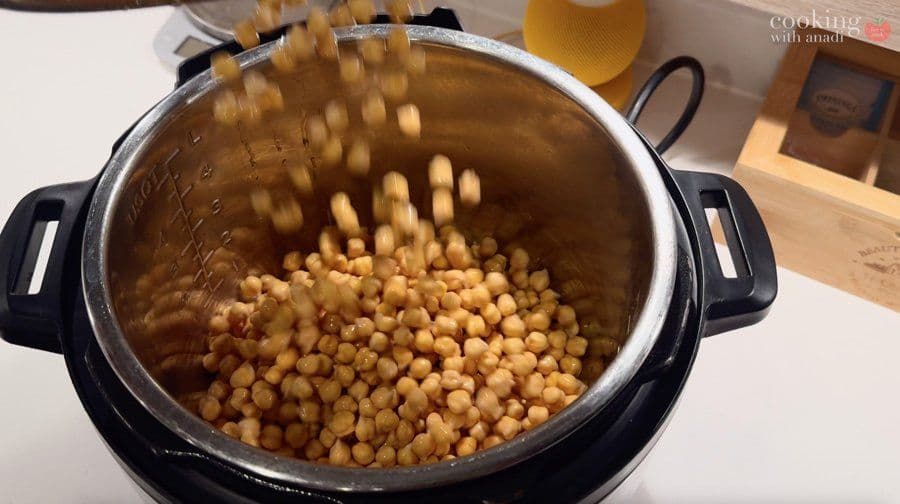 Cooked chickpeas being drained in a stainless steel strainer over an Instant Pot filled with water.