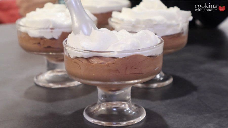 Chocolate mousse served in glass dessert cups topped with whipped cream and garnished with a spoon.