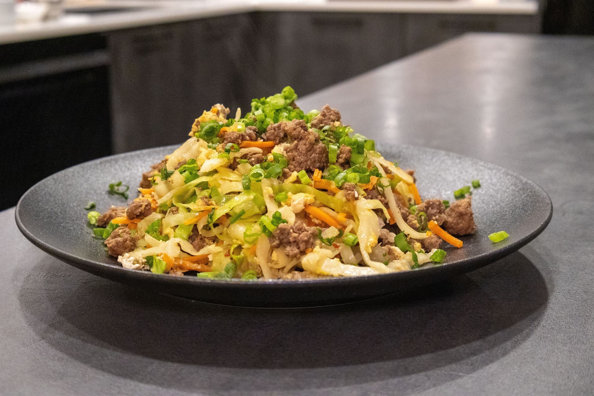 Keto egg roll in a bowl served on a black plate with ground meat, shredded cabbage, carrots, and green onions.