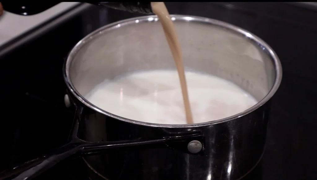 Milk steaming in a black saucepan with a wooden spoon, ready for Baileys hot chocolate.
