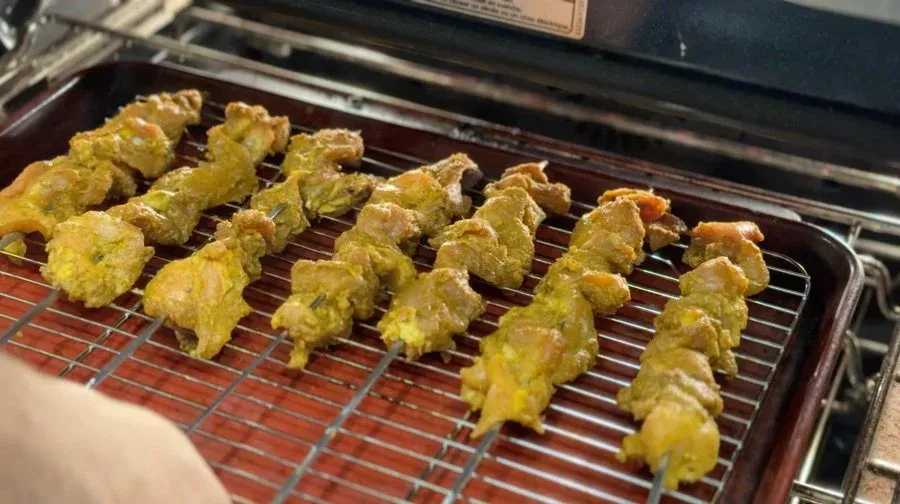 Golden-brown chicken satay skewers on a wire rack over a baking sheet during broiling.