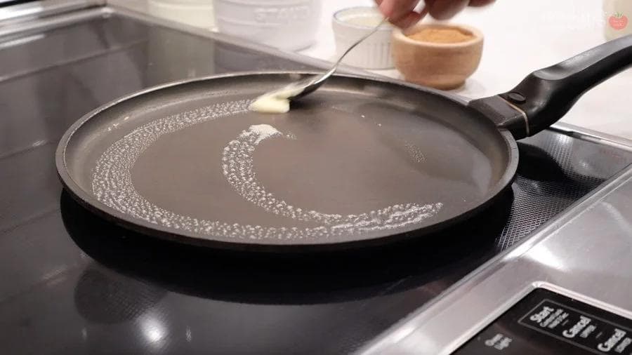 Butter being swirled in a non-stick crepe pan over medium heat on a stovetop.