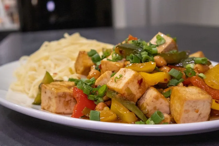 Tofu stir fry with bell peppers and green onions served over noodles on a white plate