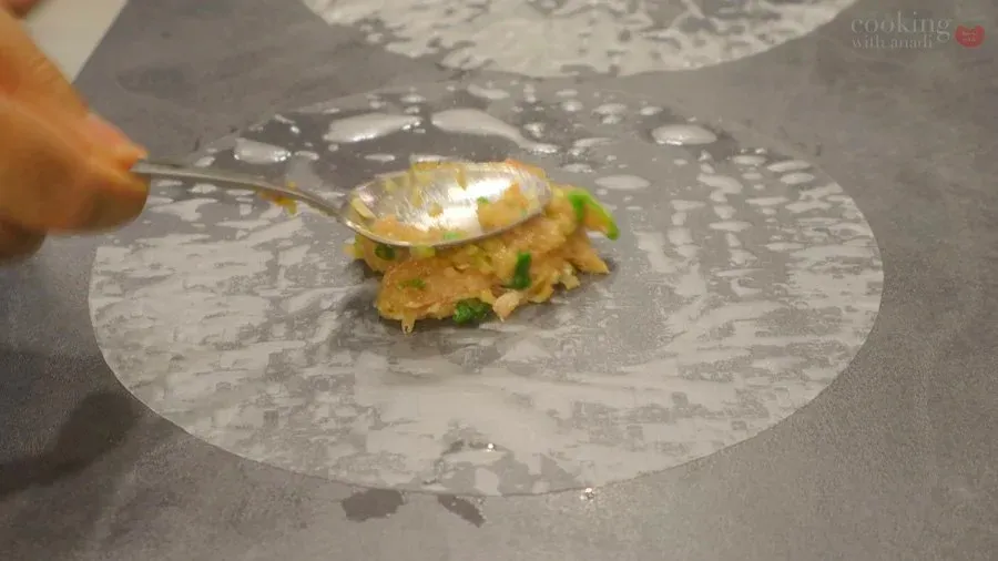 Brushing oil onto a folded rice paper dumpling filled with chicken mixture on a gray plate.