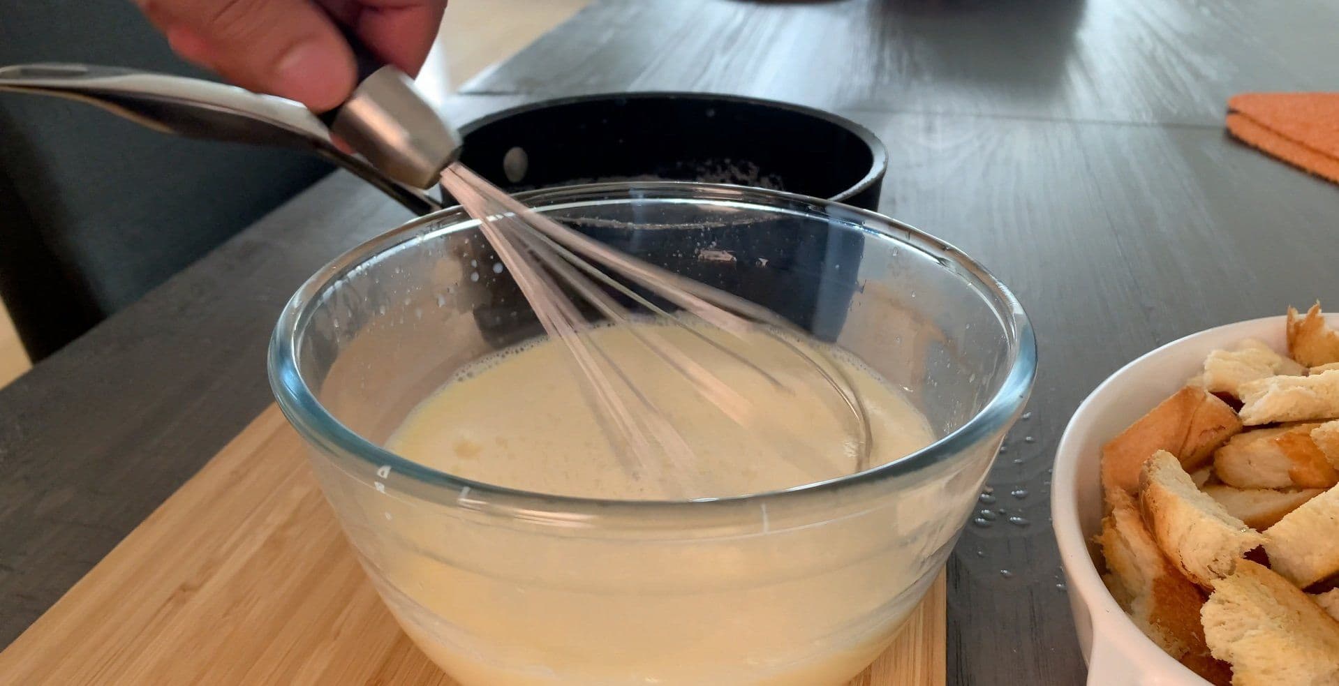 Whisking milk-egg custard mixture in a glass bowl with a whisk for bread pudding preparation.