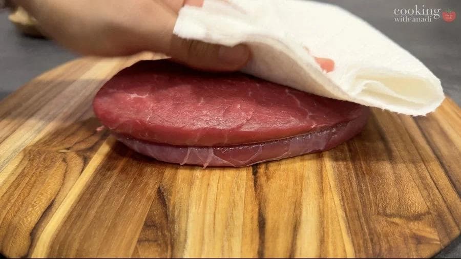 Hand brushing olive oil onto raw sirloin steak on wooden cutting board before air frying.