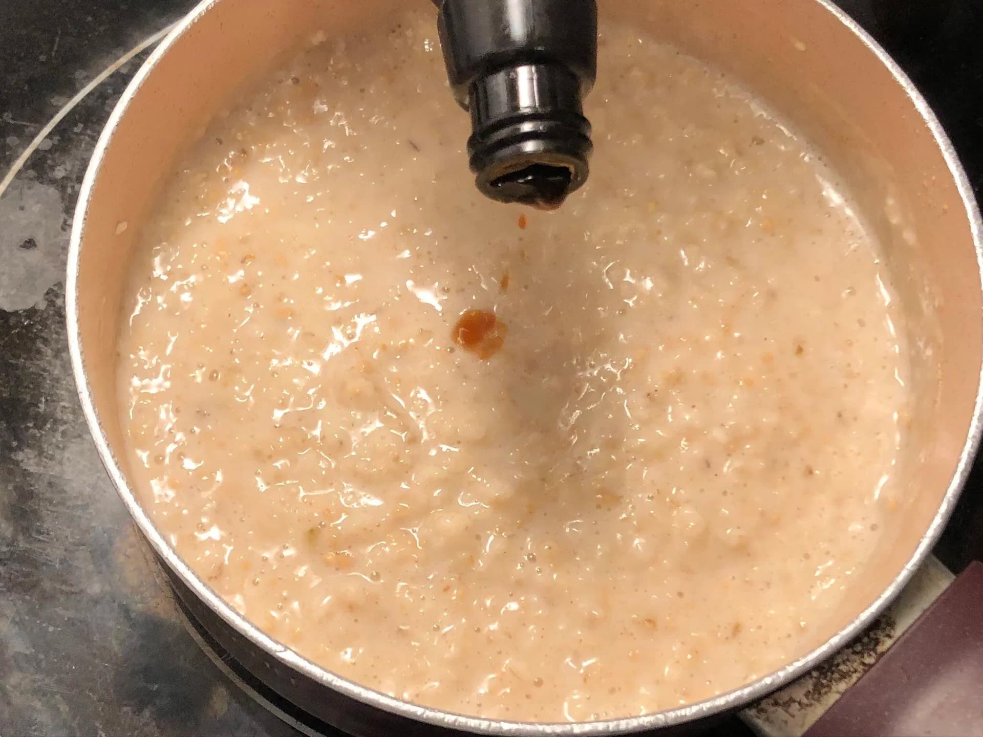 Creamy oatmeal mixture in a pot with water being added from a faucet to achieve smooth consistency.