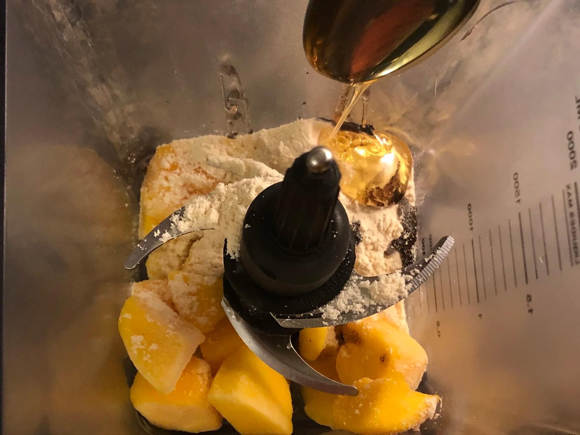 Honey being drizzled into a blender with mango chunks, vanilla paste, and flour for ice cream.