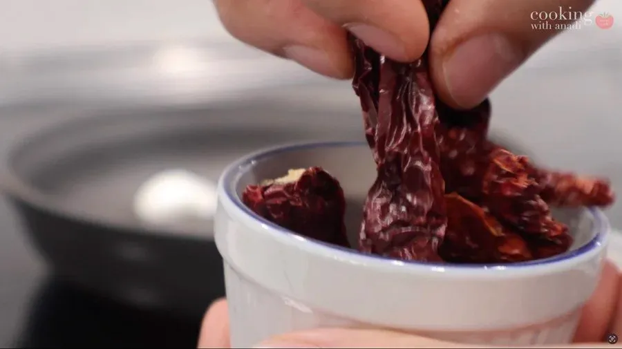 Dried red Kashmiri chilies being lifted from a bowl of water during preparation for chutney.
