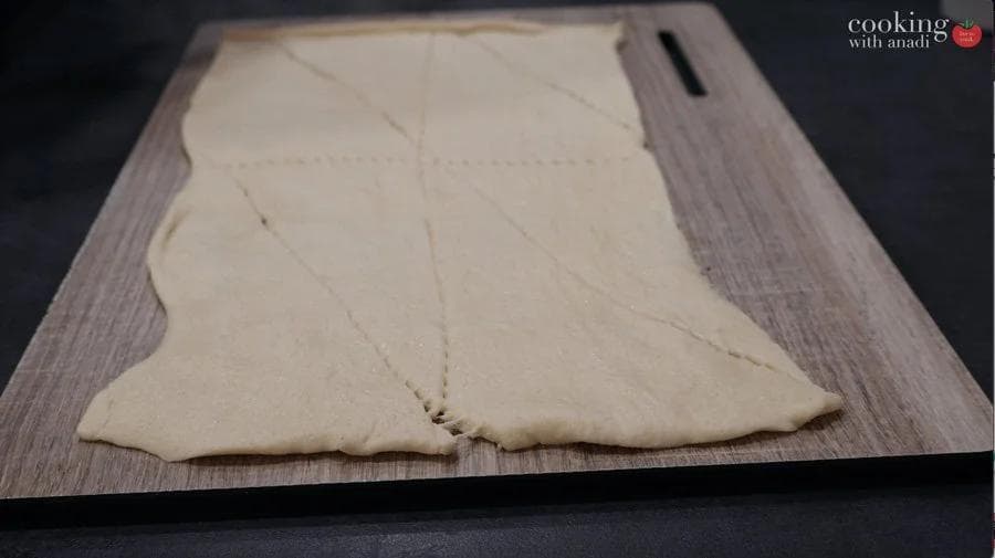 Sealed crescent roll dough sheet on a wooden board, ready to be filled with mashed potatoes.