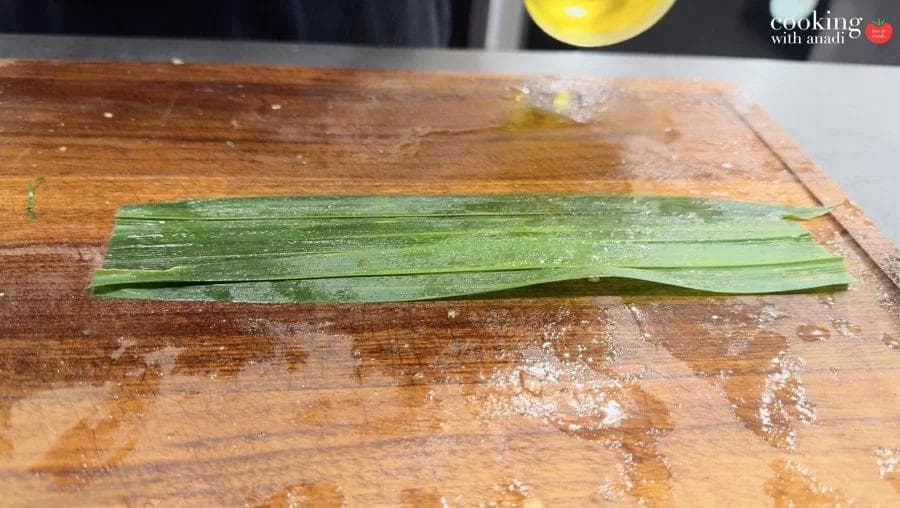 Pandan leaves laid flat and straightened on a wooden cutting board, lightly oiled and ready for wrapping.