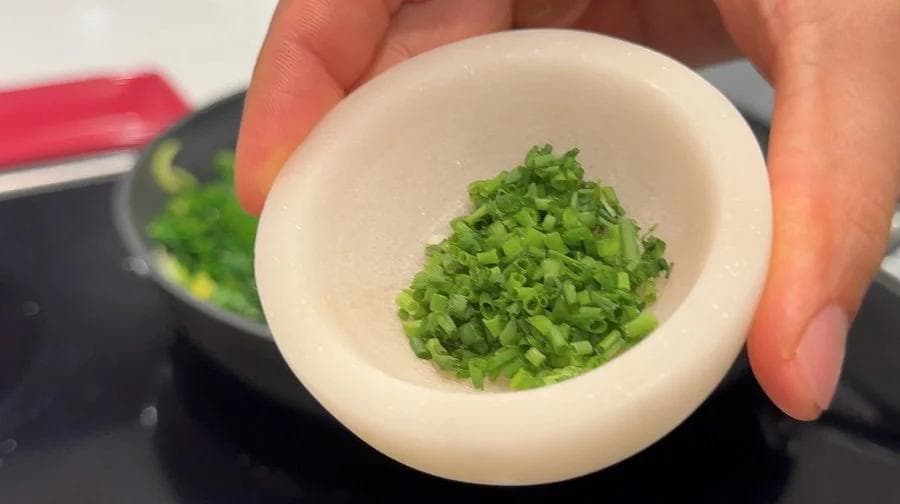 Chopped green onions and chives in a white mortar and pestle, ready to be stirred into sautéed greens.