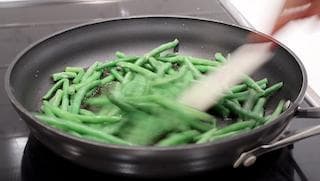 Green beans being stirred in a black skillet with a spatula during cooking on the stovetop.