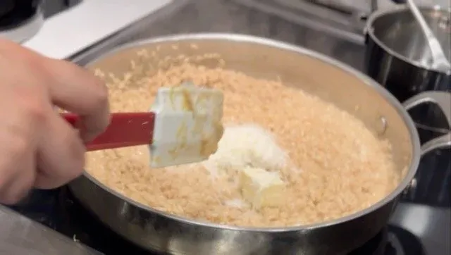 Stirring cream cheese into creamy risotto with a red spatula on the stovetop