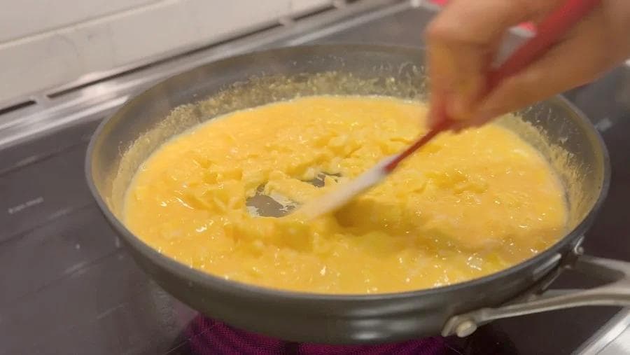 Scrambled eggs cooking in a skillet with a spatula, still slightly runny and pale yellow in color.