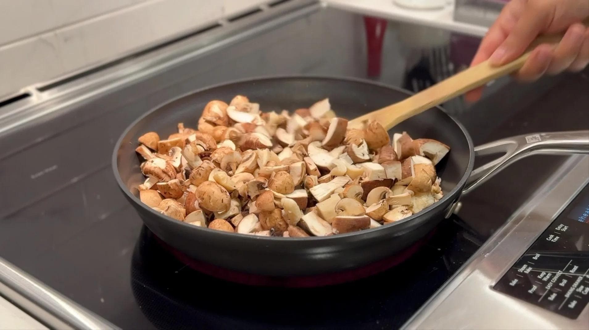 Diced mushrooms cooking in a black pan on a stovetop, being stirred with a wooden spoon.