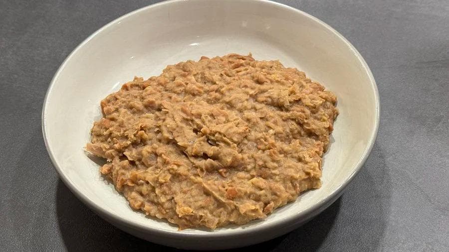 Homemade refried beans in a white bowl, showing a thick, creamy tan-brown texture with a slightly chunky appearance.