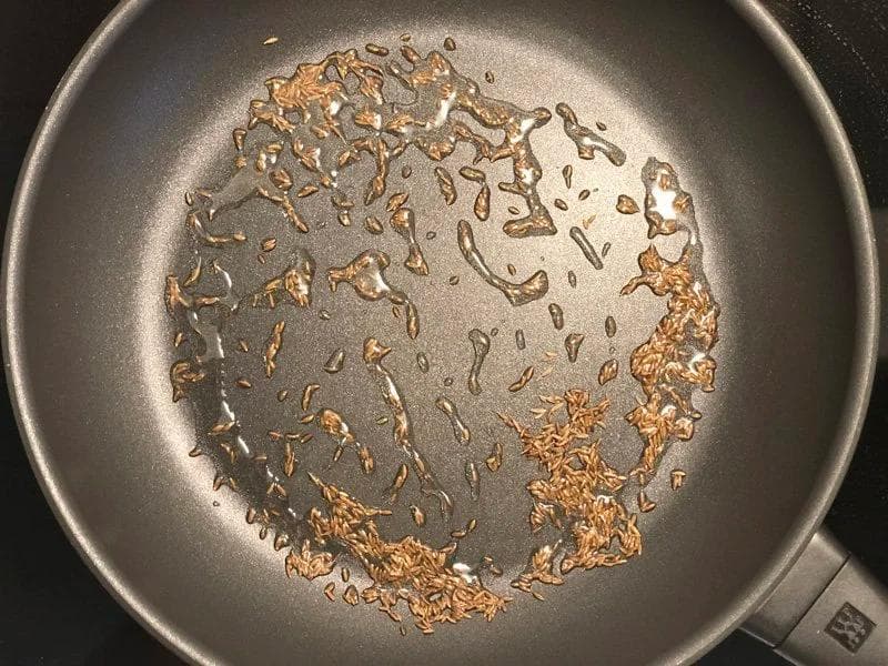 Cumin seeds crackling in oil in a pan, turning reddish brown on medium heat.