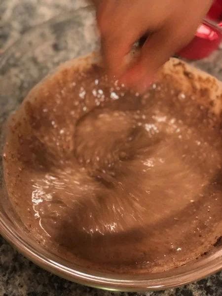 Chocolate overnight oats being stirred in a clear bowl, showing creamy cocoa-colored mixture with visible ingredients.