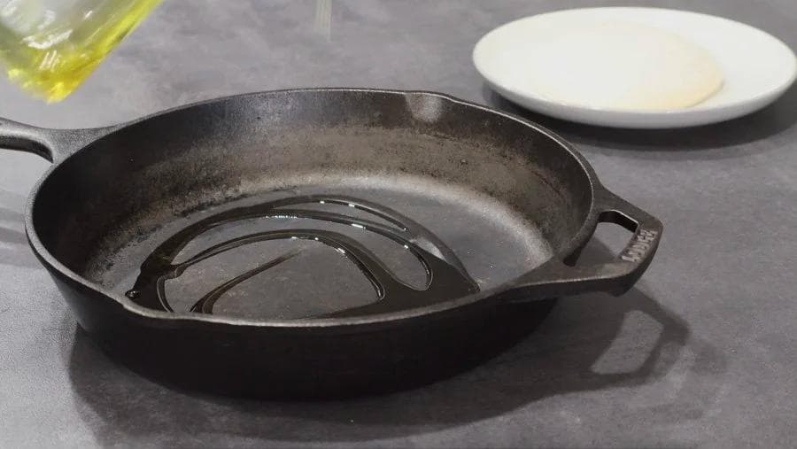 Cast iron pan coated with olive oil, ready for pizza dough to be added.