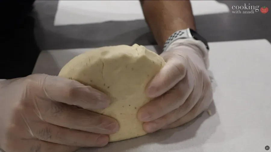 Hands kneading and stretching gluten-free dough on parchment paper into a thin, elastic sheet.