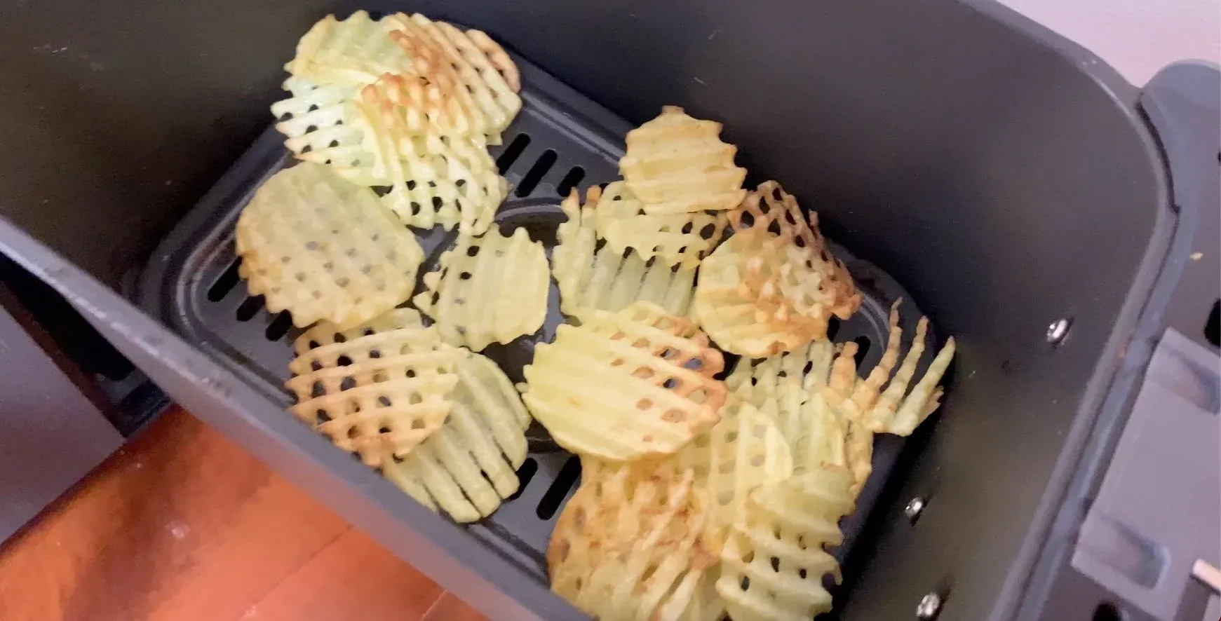 Golden waffle fries in an air fryer basket after cooking at 400F for 15 minutes.