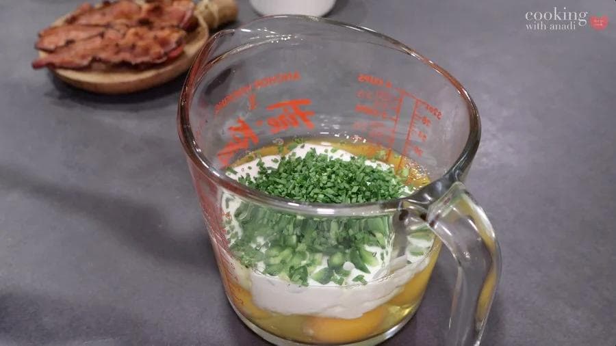 Egg muffin mixture in a measuring cup with eggs, cottage cheese, green onions, and bacon layered together.