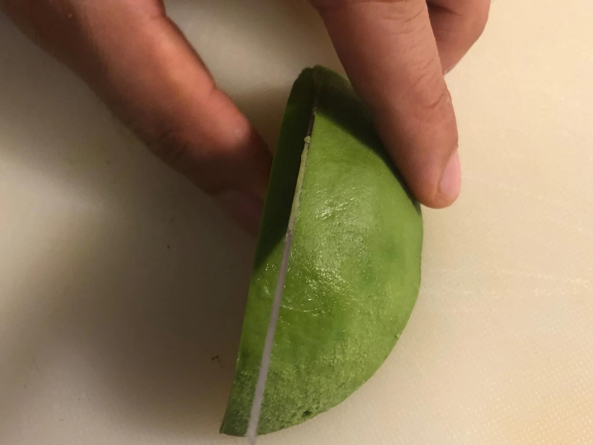Hands cutting an avocado half lengthwise with a paring knife to create an avocado fan.