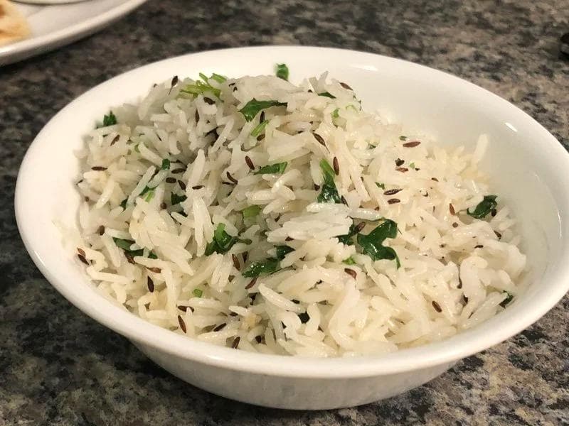Fluffy white basmati rice garnished with fresh green cilantro and cumin seeds in a white bowl.