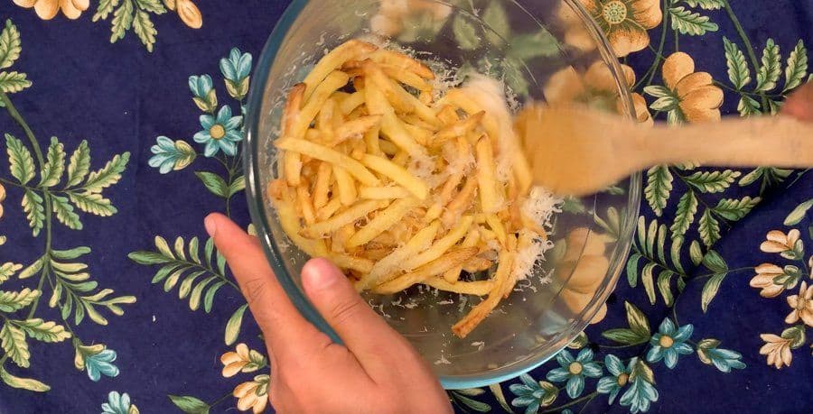 Garlic Parmesan fries tossed in a glass bowl with melted butter and grated cheese coating.