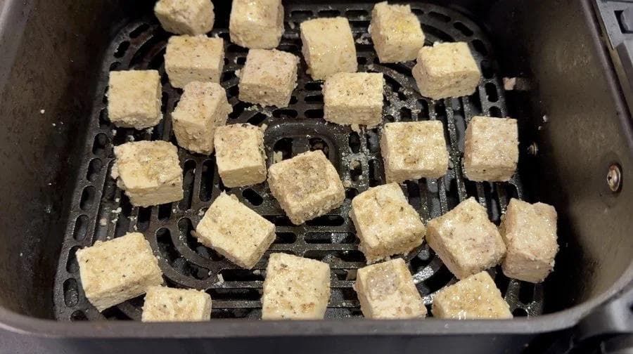 Tofu cubes arranged in a single layer in an air fryer basket before cooking.