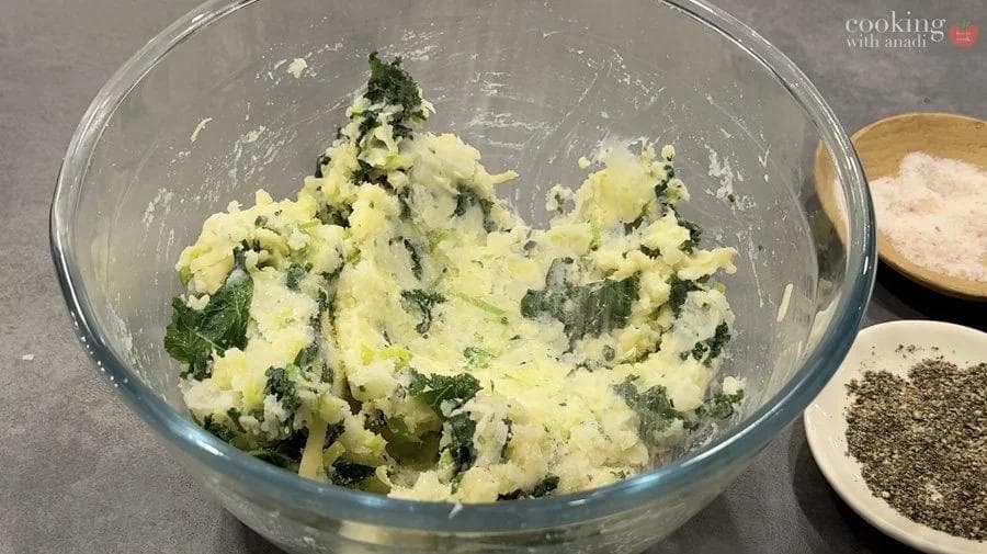 Mashed potatoes mixed with green herbs and cheese in a glass bowl, ready for stuffing.