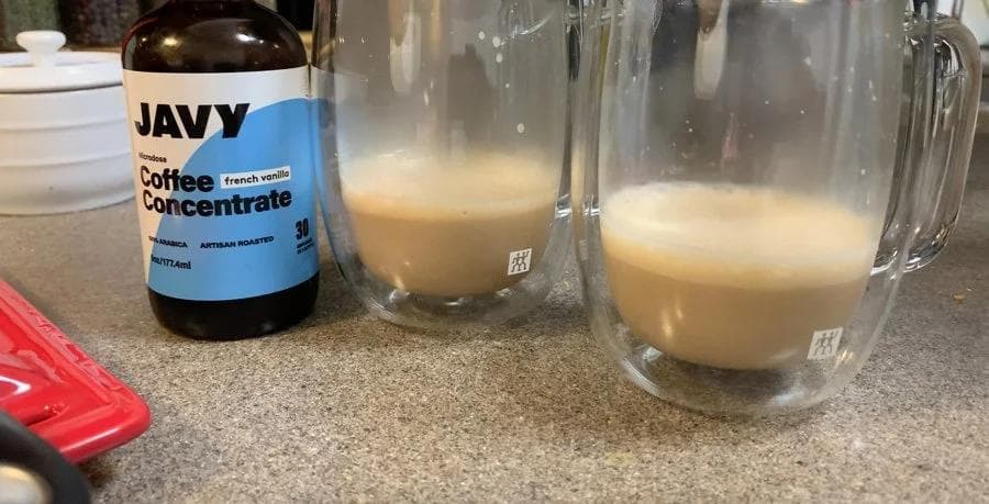 Javy coffee concentrate bottle next to two glass mugs filled with frothed white chocolate mocha.