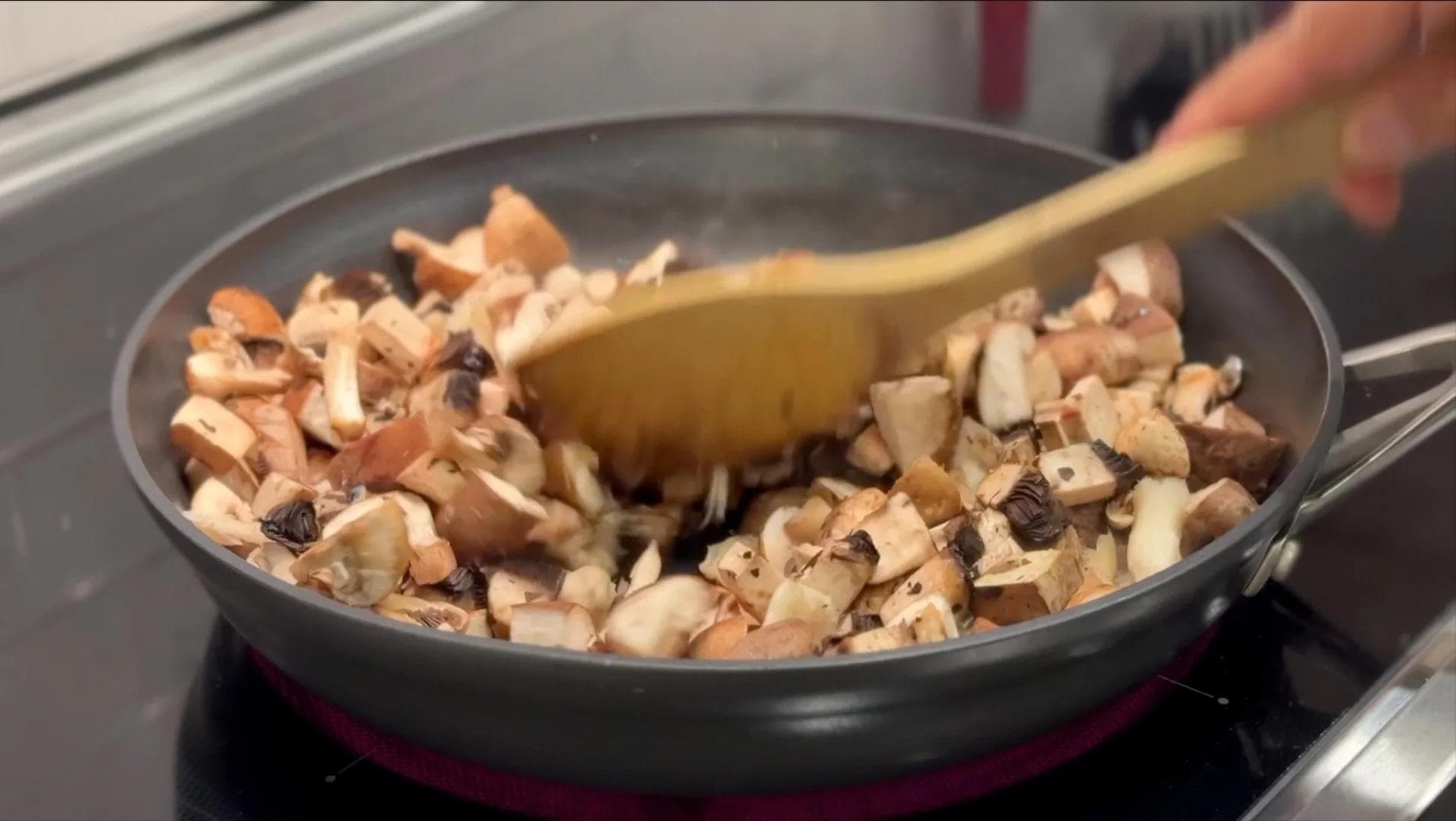 Diced mushrooms being stirred in a dark skillet with a wooden spoon on a stovetop.