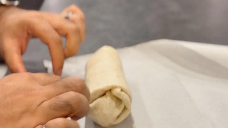 Hands wrapping a breakfast burrito in parchment paper for freezing and storage.