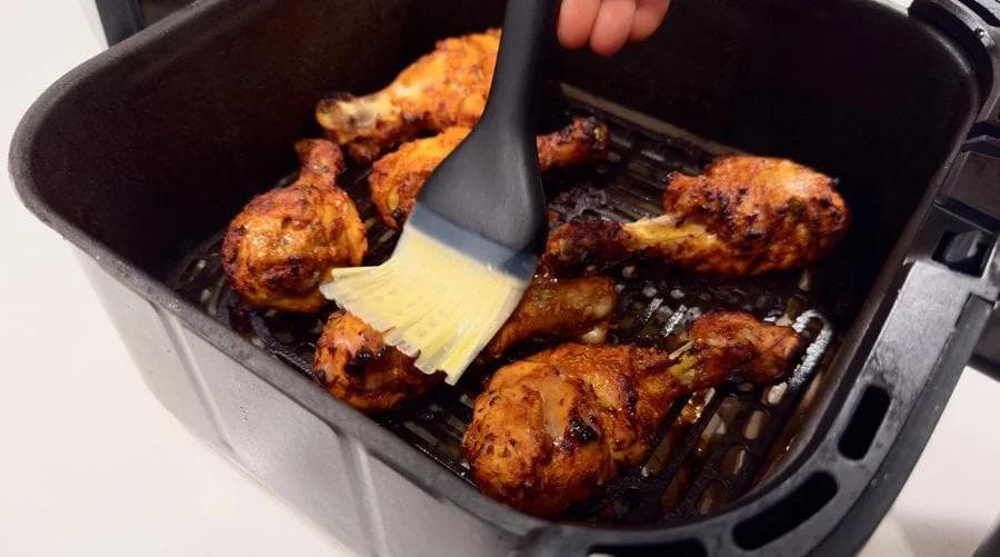 Brushing melted butter over tandoori chicken pieces in an air fryer basket during the final cooking stage.