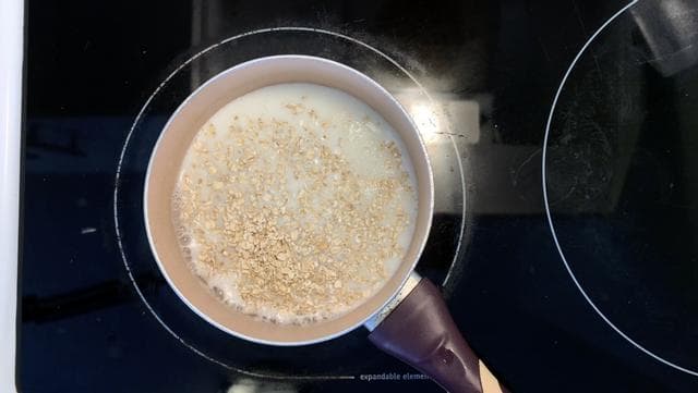 Oats simmering in milk with carrot puree stirred into a creamy mixture in a saucepan.