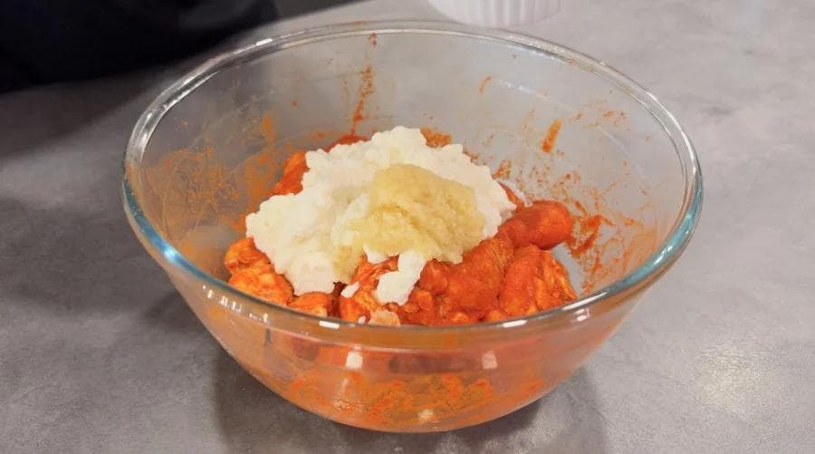 Glass bowl with red tandoori marinade and dollops of yogurt and ginger-garlic paste on top, ready to mix.