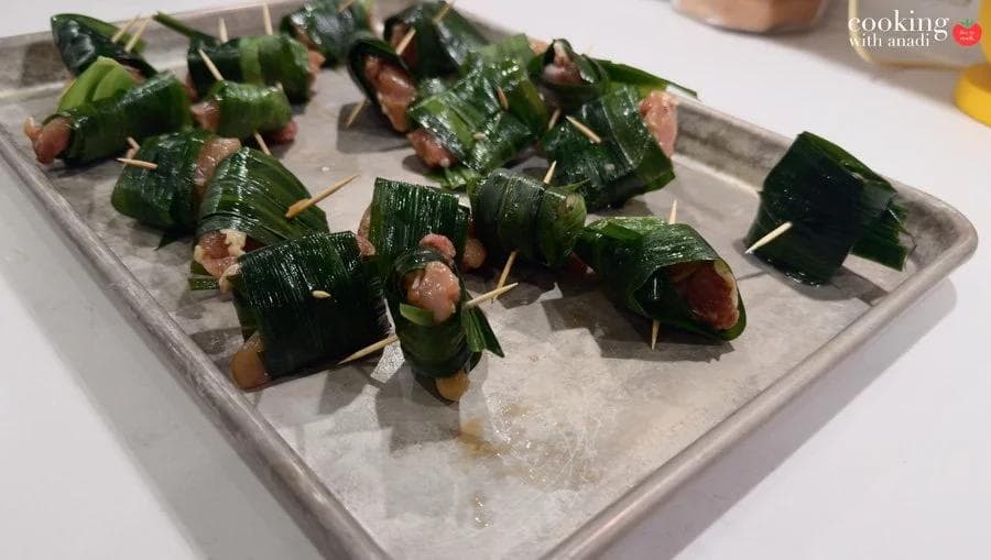 Pandan leaf-wrapped chicken pieces secured with toothpicks, arranged on a parchment-lined baking sheet, ready to air fry.
