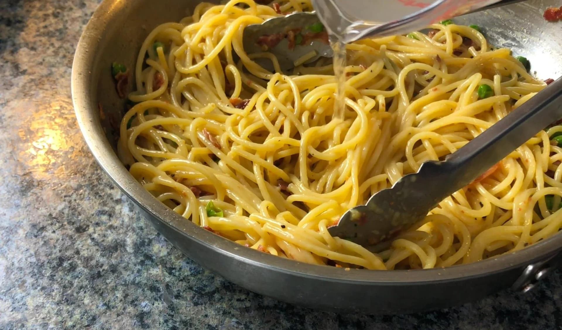 Spaghetti alla carbonara being stirred in a pan with a creamy sauce coating the noodles.