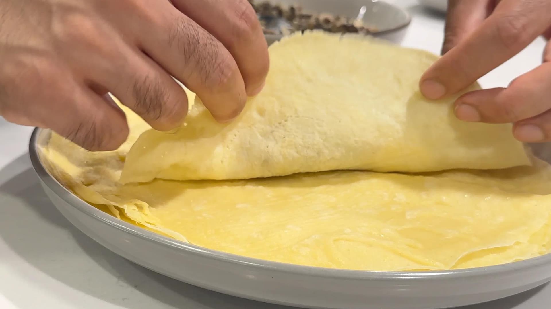 Hands folding a yellow crepe filled with mushroom-sauerkraut filling on a white plate.