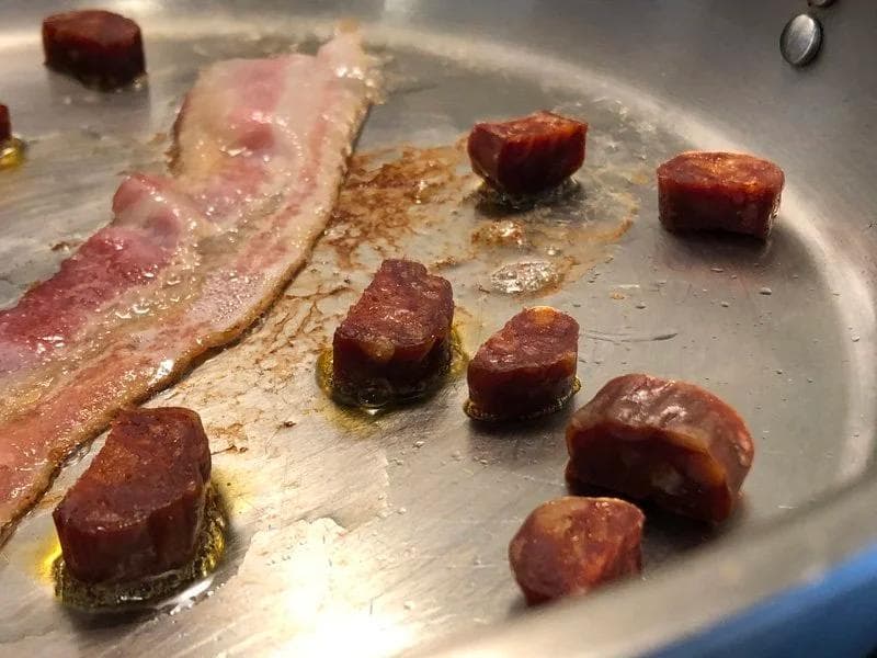 Bacon strips and diced chorizo cooking in a skillet until crispy and browned.