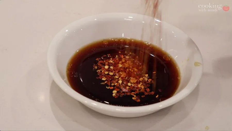 Dark brown stir fry sauce with red chili flakes in a white bowl, ready to use.