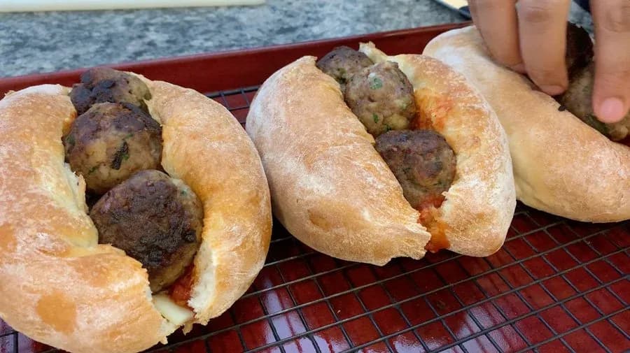 Three assembled meatball subs on a red cooling rack with mozzarella and marinara sauce visible.